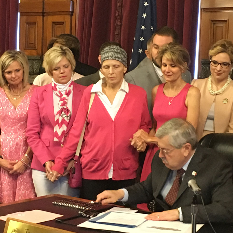 Governor Branstad signing Patty's Law as advocates in pink hold hands behind him