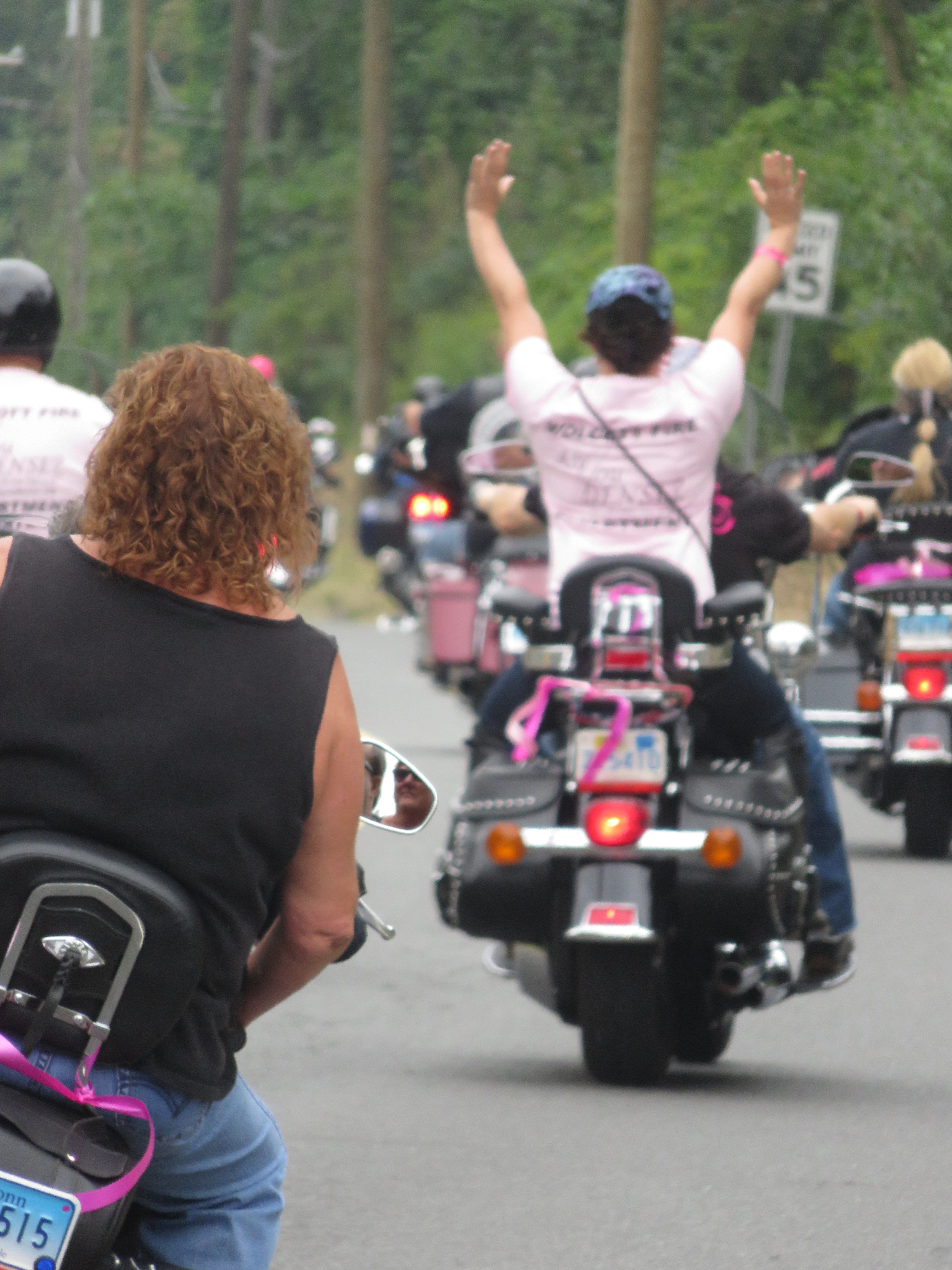 Rider raising both arms in celebration from the back of a motorcycle during the ride