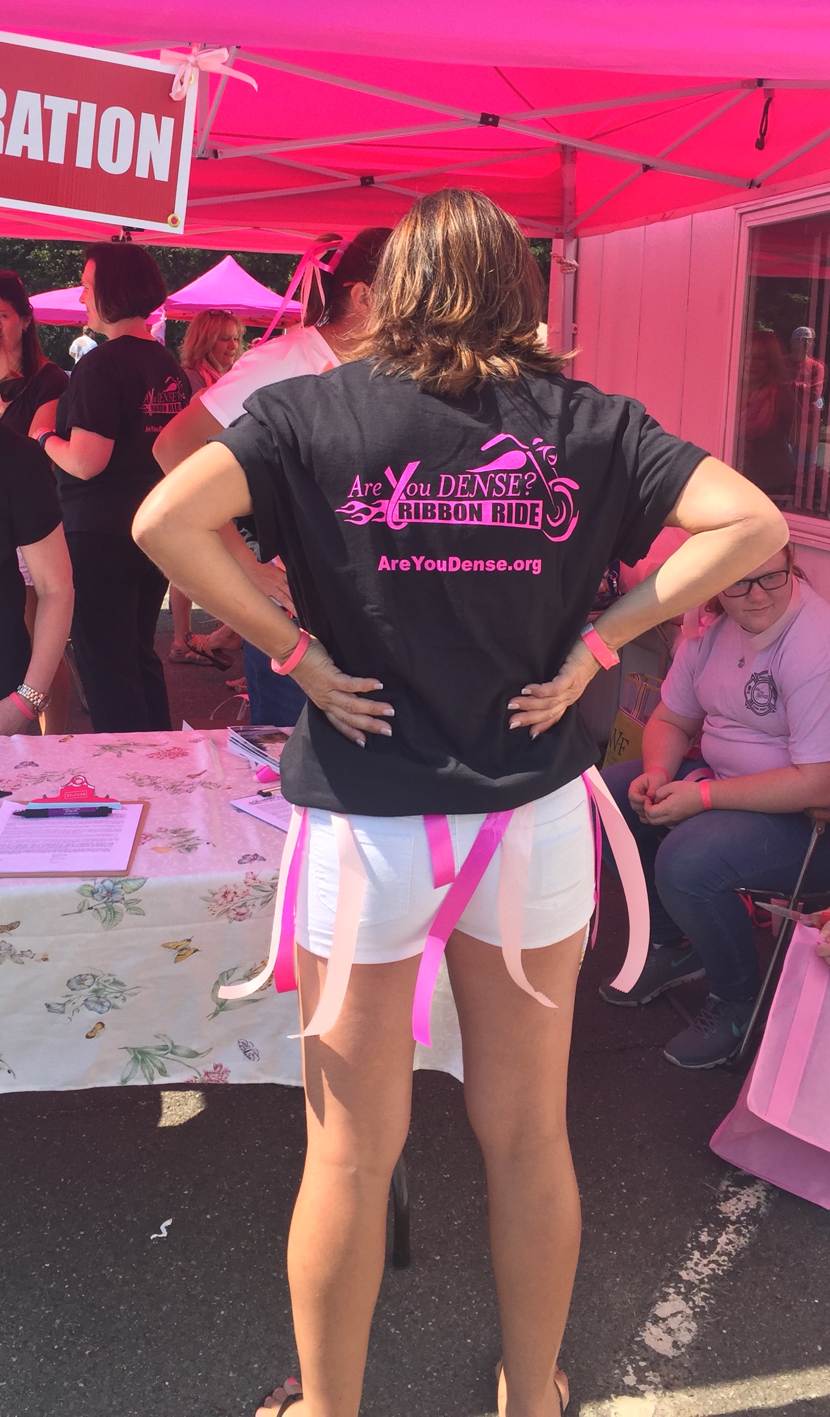 Volunteer at registration showing the back of an Are You Dense? Ribbon Ride T-shirt