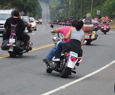 Riders heading down the road, a passenger in pink behind one of the motorcyclists