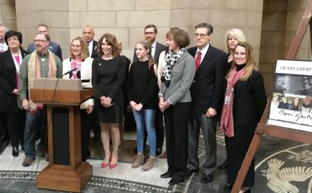 Group standing beside a podium and an LB 195 Cheri's Law poster at the Nebraska Capitol