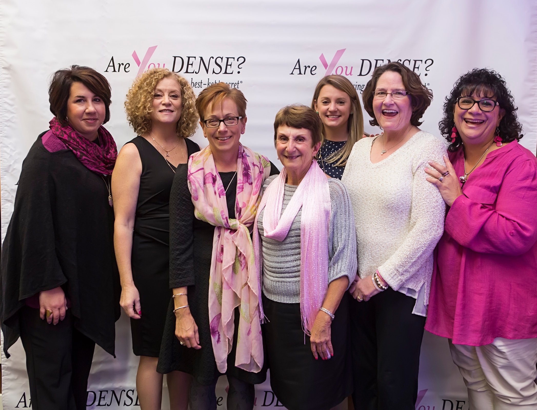 Seven guests posing at the Are You Dense? backdrop at For the Girls 2016
