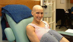 Dr. Nancy Cappello, bald from treatment, smiling in a treatment chair