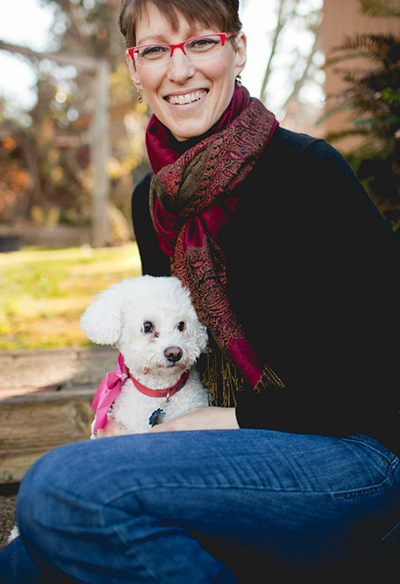 Laura Caldwell smiling outdoors with her small white dog
