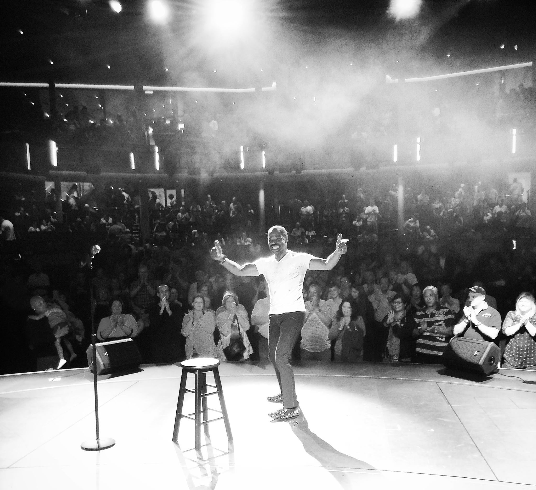 Kenny James with arms raised on stage before a cheering theater audience