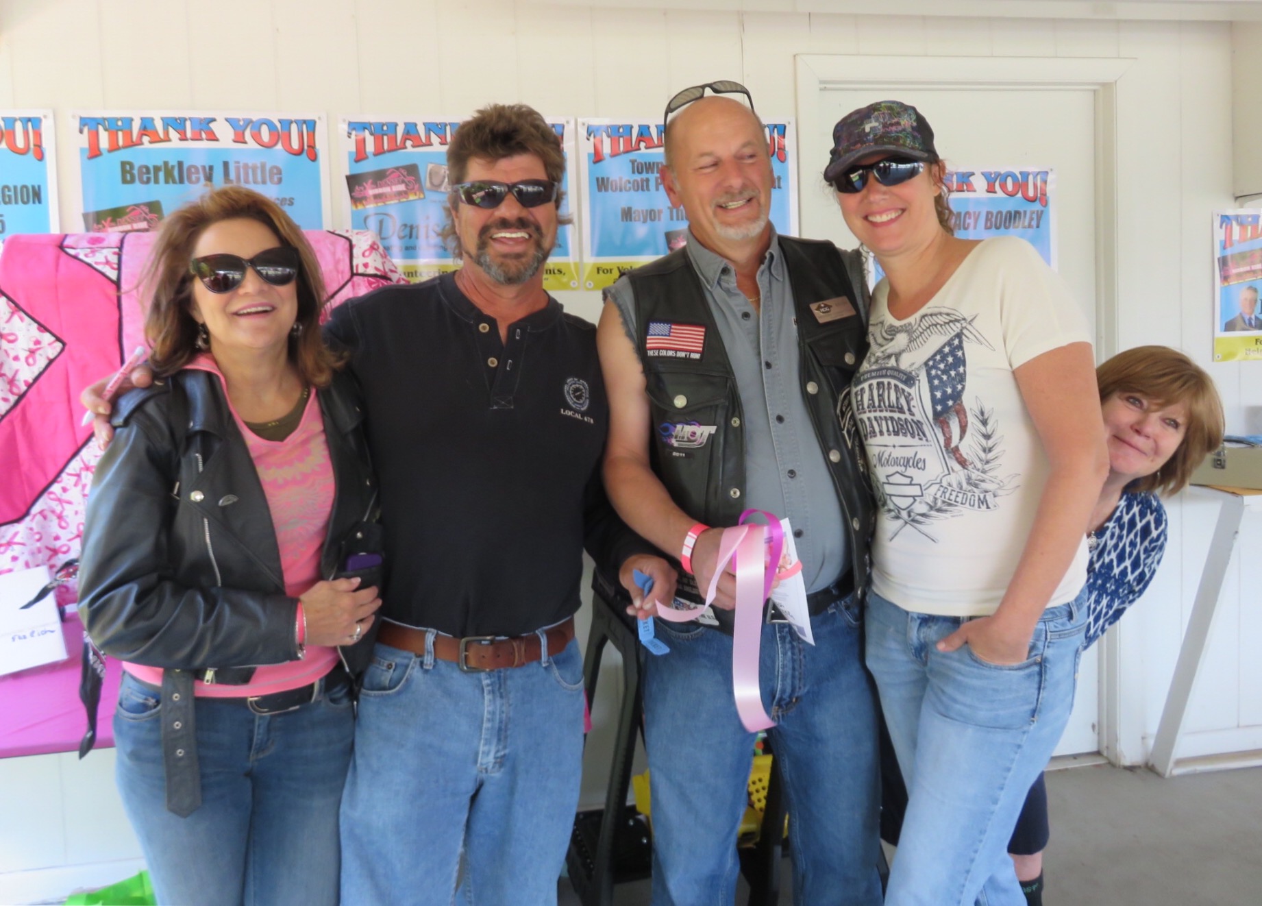 Five supporters, one holding pink ribbons, smiling in front of thank-you signs