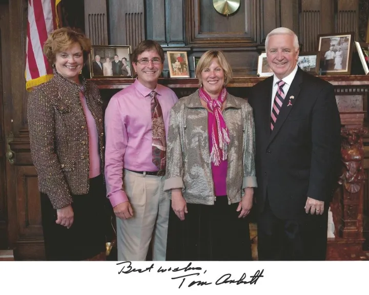 Four people in a formal office before a US flag, signed “Best wishes, Tom Corbett”